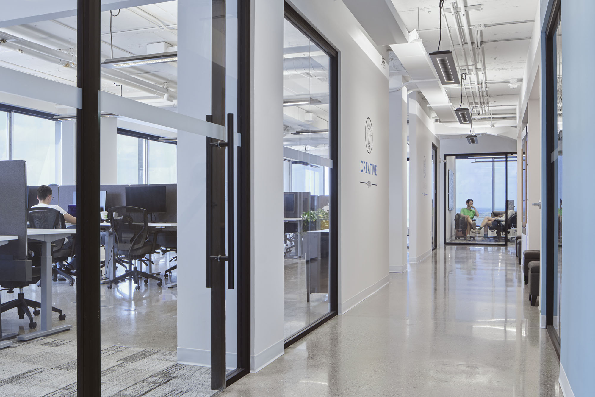 hallway of office with people working at desks and meetings